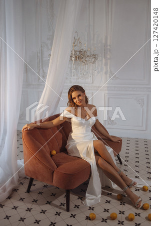 Woman in white dress sitting on terracotta sofa in classic white room with lemons on the floor 127420148