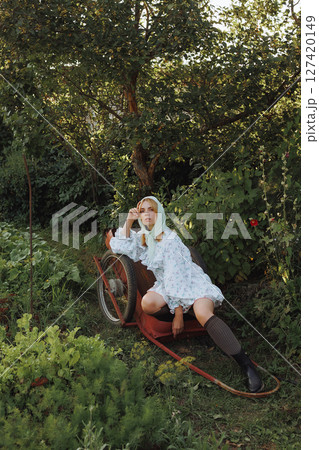 A fashionable woman poses on a red wheelbarrow in the garden 127420149