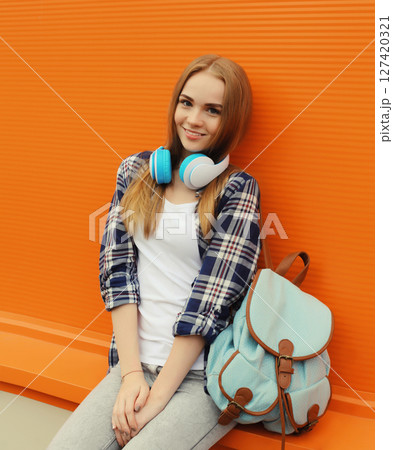 happy young woman listening to music with headphones, modern teenage girl with backpack in the city 127420321