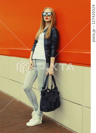 Stylish young woman standing in black leather jacket, sunglasses, modern blonde girl posing in city Stylish young woman standing in black leather jacket, sunglasses, modern blonde girl posing in city 127420324