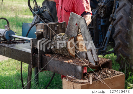 Farmer operating a tractor powered log splitter, splitting firewood logs for winter heating, showcasing traditional methods of wood preparation in rural areas 127420478