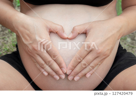 Pregnant woman forming a heart shape with her hands on her belly, radiating love and connection with her unborn child, symbolizing the deep bond of motherhood and anticipation 127420479