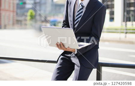 ビジネス街でノートパソコンを見るスーツの若い男性 ビジネス街でノートパソコンを見るスーツの若い男性 127420598