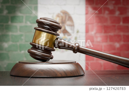 Wooden Gavel Resting on Table In Front of A Brick Wall with Mexican Flag. 127420783