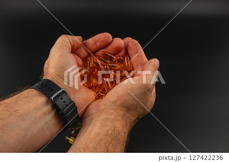 Hands holding various orange capsules on a dark surface 127422236