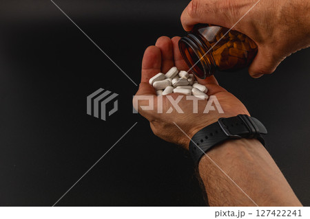Hands pouring white pills from a bottle into palm Hands pouring white pills from a bottle into palm 127422241