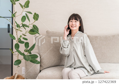 スマホで電話する日本人女性(家・ソファ・笑顔) スマホで電話する日本人女性(家・ソファ・笑顔) 127422369