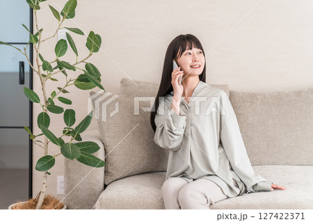 スマホで電話する日本人女性（家・ソファ・笑顔） 127422371