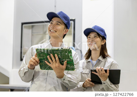 工場でタブレットを使って製品を検査する男女作業員 127422766