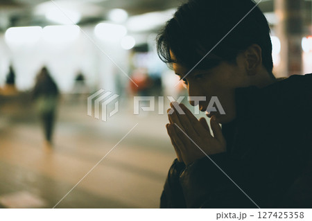 寒さで手に息を吹きかける20代男性 寒さで手に息を吹きかける20代男性 127425358