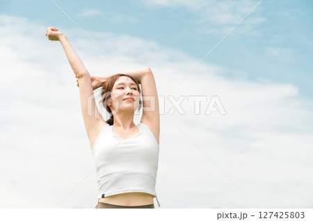 青空の下でストレッチするヨガウェアの女性（運動・深呼吸・日光浴・リフレッシュ・ストレス解消） 127425803