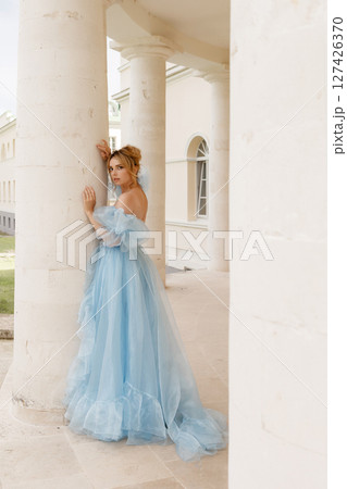 Elegant woman in blue ball gown posing near white stone column 127426370