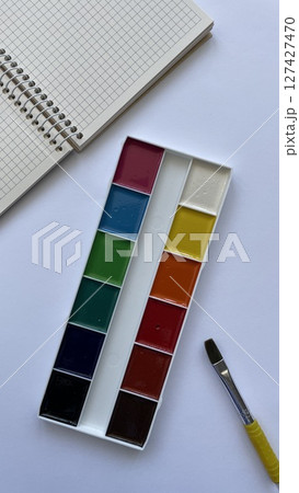 Top View of Watercolor Paint Set with Brush and Spiral Notebook on White Background. Artistic Supplies for Back to School and Creativity. Top View of Watercolor Paint Set with Brush and Spiral Notebook on White Background. Artistic Supplies for Back to School and Creativity. 127427470