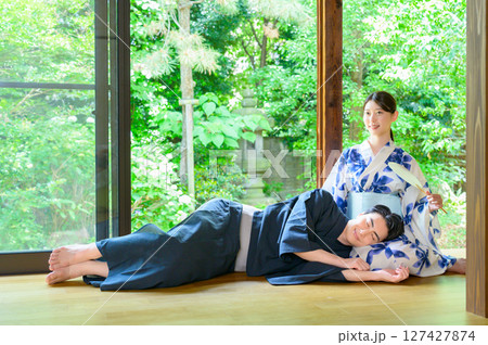 縁側に寝転ぶ男性と浴衣姿の女性が寄り添いながら静かな時間を共に過ごす夏の風景 127427874