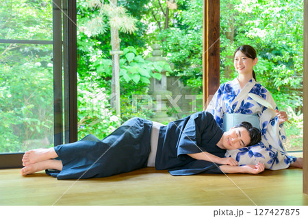 窓からの緑を背景に膝枕で休む男性と微笑む女性が過ごす日本の夏のやさしい縁側風景 127427875
