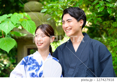 うちわを持った女性と笑顔の男性が浴衣で並び自然豊かな庭園でゆったり過ごす夏の休日風景 127427918