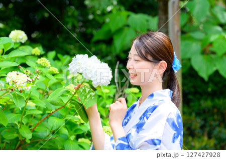 浴衣姿の女性が紫陽花の前で目を閉じながらゆったりと夏の香りを楽しむ穏やかなガーデン風景 127427928