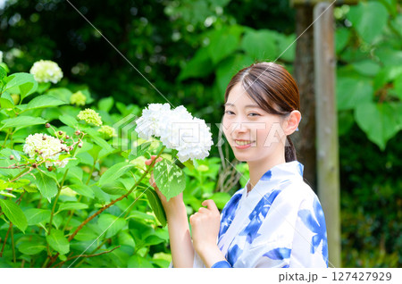 夏の庭園で浴衣を着た女性が紫陽花をそっと眺めながら優雅に微笑む清涼感ある自然ポートレート 127427929