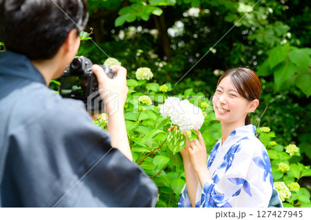 笑顔を見せる浴衣女性を男性が撮影する庭園でのやりとりを捉えた夏のスナップポートレート 127427945
