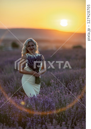 Blonde woman poses in lavender field at sunset. Happy woman in white dress holds lavender bouquet. Aromatherapy concept, lavender oil, photo session in lavender Blonde woman poses in lavender field at sunset. Happy woman in white dress holds lavender bouquet. Aromatherapy concept, lavender oil, photo session in lavender 127428705