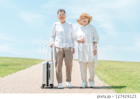 スーツケースを持って仲良く歩く旅行中のおしどり夫婦 スーツケースを持って仲良く歩く旅行中のおしどり夫婦 127429125