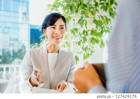 明るい室内で顧客にプレゼンテーション資料の説明をして営業する30代の笑顔の女性 明るい室内で顧客にプレゼンテーション資料の説明をして営業する30代の笑顔の女性 127429179