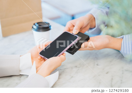 お店でコーヒーをスマートフォンのタッチ決済で購入する女性の手元 127429180