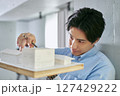 建物の模型を作って家の設計を行う建築学科で勉強をする1人の大学生の男性 建物の模型を作って家の設計を行う建築学科で勉強をする1人の大学生の男性 127429222