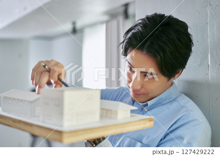 建物の模型を作って家の設計を行う建築学科で勉強をする1人の大学生の男性 建物の模型を作って家の設計を行う建築学科で勉強をする1人の大学生の男性 127429222