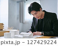 建物の模型と図面を見て建築の設計図を確認するデザイン事務所で働く1人の設計士の男性 建物の模型と図面を見て建築の設計図を確認するデザイン事務所で働く1人の設計士の男性 127429224