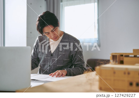 建築を設計する事務所で模型と図面を前に真剣に働く建築士の1人の男性 127429227