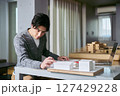 建築模型を眺めながらノートパソコンと手元の図面で建物の意匠の設計の勉強をする建築学科の男性の学生 建築模型を眺めながらノートパソコンと手元の図面で建物の意匠の設計の勉強をする建築学科の男性の学生 127429228