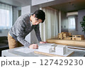 建築模型の置かれたデスクで設計図を確認し作図しながら設計を行う建築士の男性 建築模型の置かれたデスクで設計図を確認し作図しながら設計を行う建築士の男性 127429230
