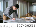 アトリエ系の設計事務所の建物の模型が置かれたデスクで立って図面を書く建築士の所員の男性 アトリエ系の設計事務所の建物の模型が置かれたデスクで立って図面を書く建築士の所員の男性 127429231