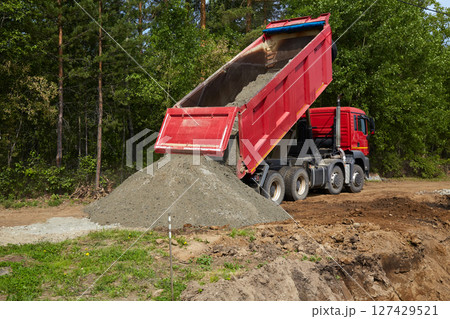 A dump truck tilts to pour gravel onto the ground at a construction site 127429521
