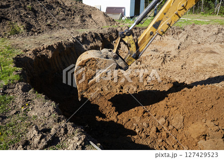 A digger operates in a rural setting, carefully excavating a deep trench. A digger operates in a rural setting, carefully excavating a deep trench. 127429523