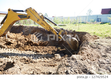 An excavator works in rural areas, carefully digging a deep excavation for the construction of a house. 127429524