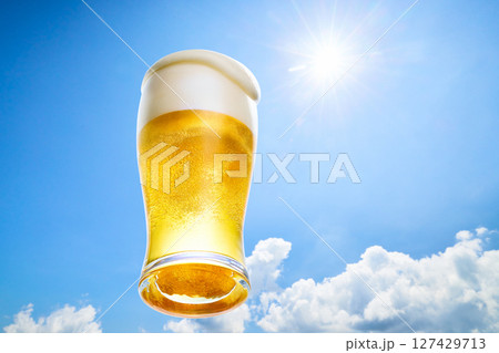 冷えたビールの泡がグラスからこぼれ落ちる、夏の青空に太陽の光の背景 127429713