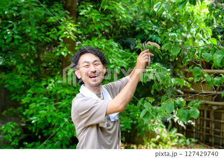 剪定作業中の男性が満面の笑みを浮かべながら自然と向き合う和やかな夏の庭園風景 127429740