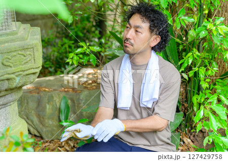 白い手袋をはめた男性が石灯籠の前で作業開始前に気持ちを整えるように静かに座る場面 127429758