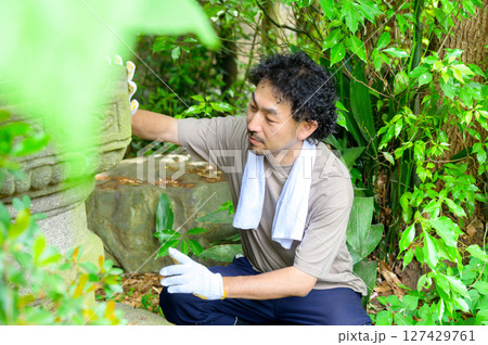 白い手袋をつけた男性が石灯籠を手で優しくなぞりながら苔や汚れを確認する庭園整備の一幕 127429761