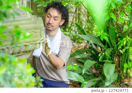 石灯籠を正面から見つめながら両手でゆっくり触れて状態を確かめる男性の落ち着いた作業風景 127429771