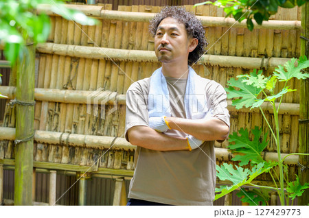 竹垣の前で腕を組みながら作業エリアをじっと見つめる男性が次の工程を考える思案の表情 127429773