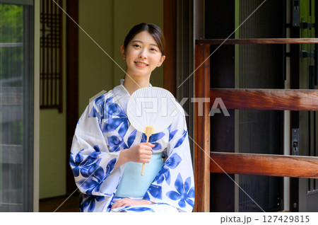 和風旅館の縁側で浴衣を着た女性が白いうちわを両手に持ち涼しげな表情で過ごす夏の一場面 和風旅館の縁側で浴衣を着た女性が白いうちわを両手に持ち涼しげな表情で過ごす夏の一場面 127429815