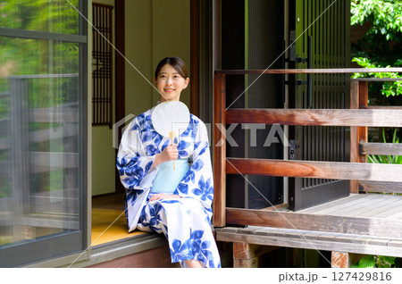 縁側に腰掛けた浴衣姿の女性が涼しげにうちわを手に持ち夏の風景に溶け込む和の暮らしのひととき 縁側に腰掛けた浴衣姿の女性が涼しげにうちわを手に持ち夏の風景に溶け込む和の暮らしのひととき 127429816