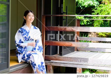 縁側で浴衣を着た女性が笑顔で外を見つめながら夏の午後を過ごす穏やかな癒しのワンシーン 縁側で浴衣を着た女性が笑顔で外を見つめながら夏の午後を過ごす穏やかな癒しのワンシーン 127429819