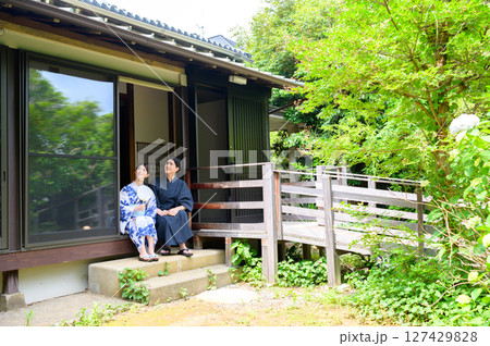 木造旅館の縁側で浴衣の男女が並んで座りながら穏やかな夏の午後を共有する和の暮らしの風景 127429828