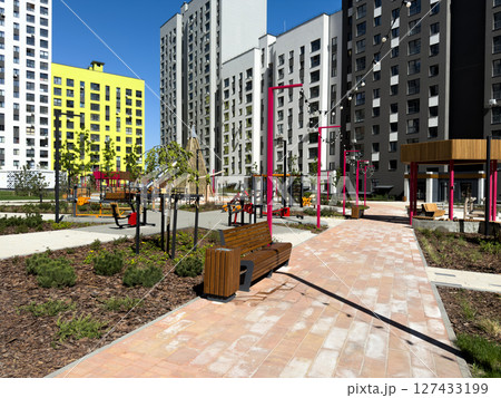 Modern landscaped courtyard in residential complex with workout area, playground, benches and decorative lighting, offering safe and comfortable space for urban living and family leisure Modern landscaped courtyard in residential complex with workout area, playground, benches and decorative lighting, offering safe and comfortable space for urban living and family leisure 127433199