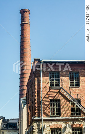 Tall red brick chimney and industrial building in sunlight against blue sky. High quality photo 127434486