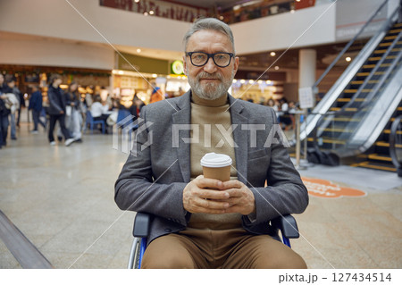 A stylish man enjoys his coffee while relaxing in a wheelchair at a modern mall setting 127434514